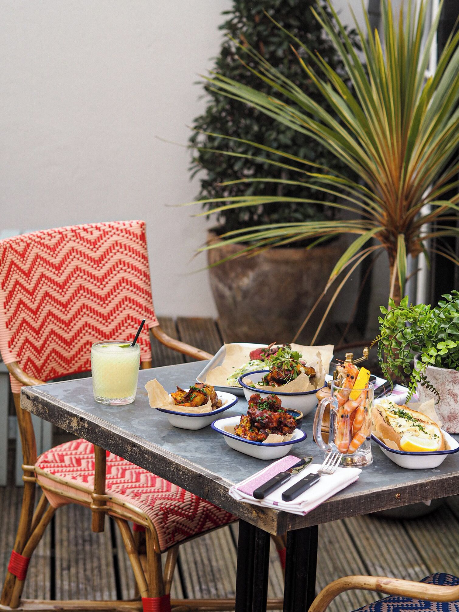 A dining table with various dishes, a drink, and a chair with a patterned cushion.