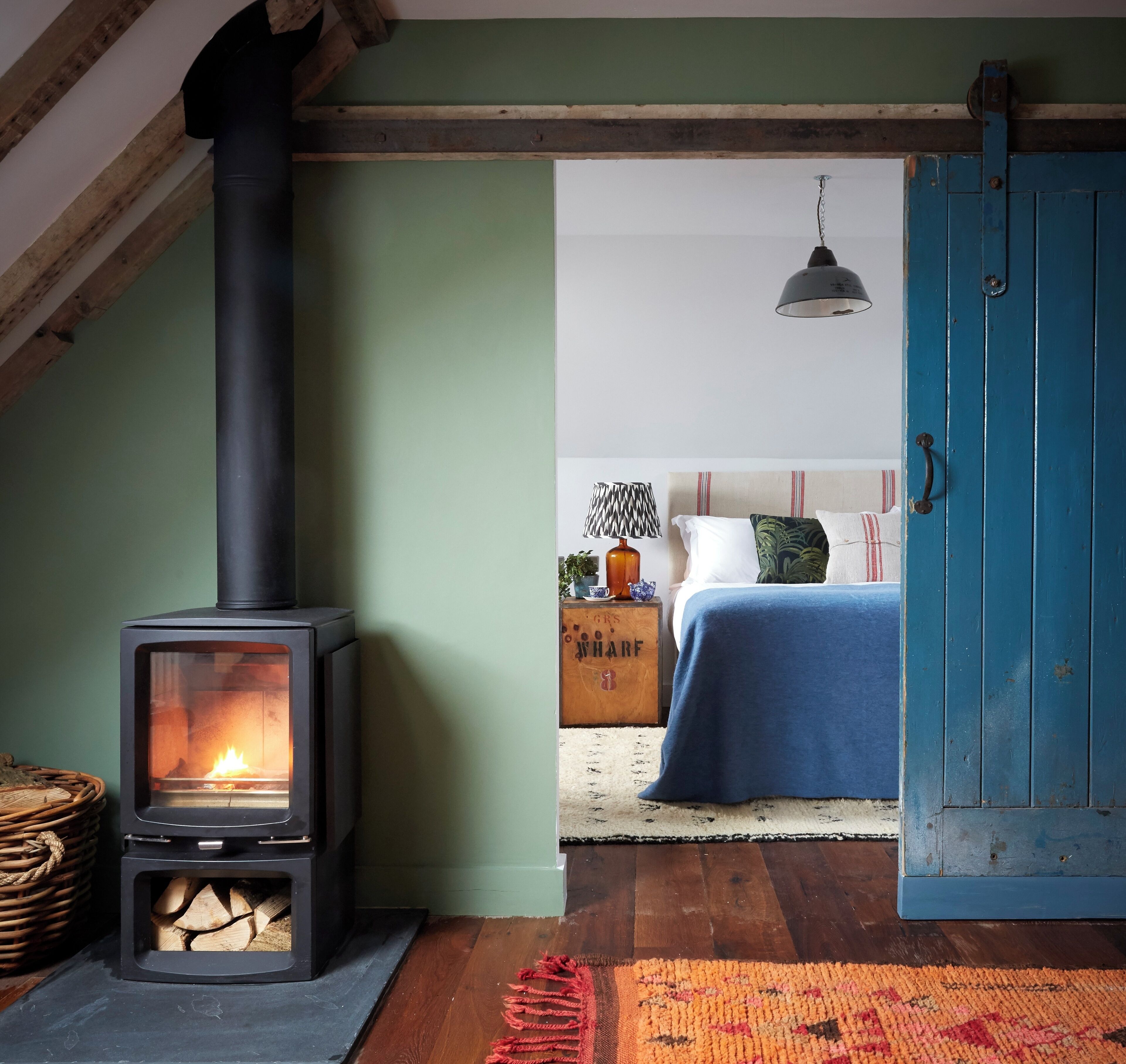 Una habitación acogedora con una estufa de leña, una cama con manta azul y una puerta azul.