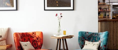 Una sala de estar acogedora con dos sillones estampados, una mesita de madera con un florero y cuadros en la pared.