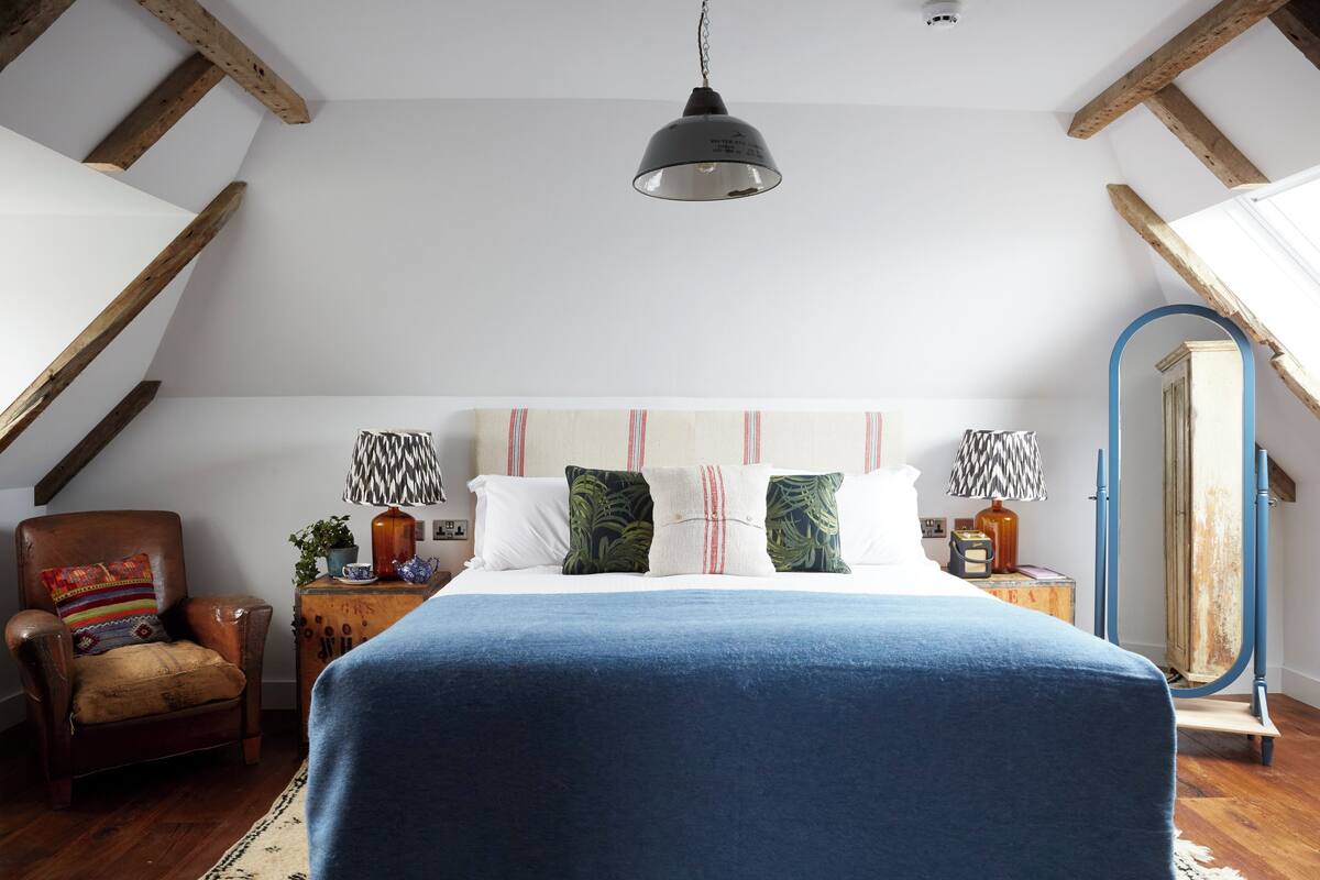 A bedroom with a large bed, a wooden chair, a small table with a lamp, and a mirror on the wall.
