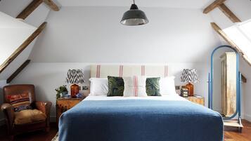 Een slaapkamer met een groot bed, een houten stoel, een klein tafeltje met een lamp en een spiegel aan de muur.