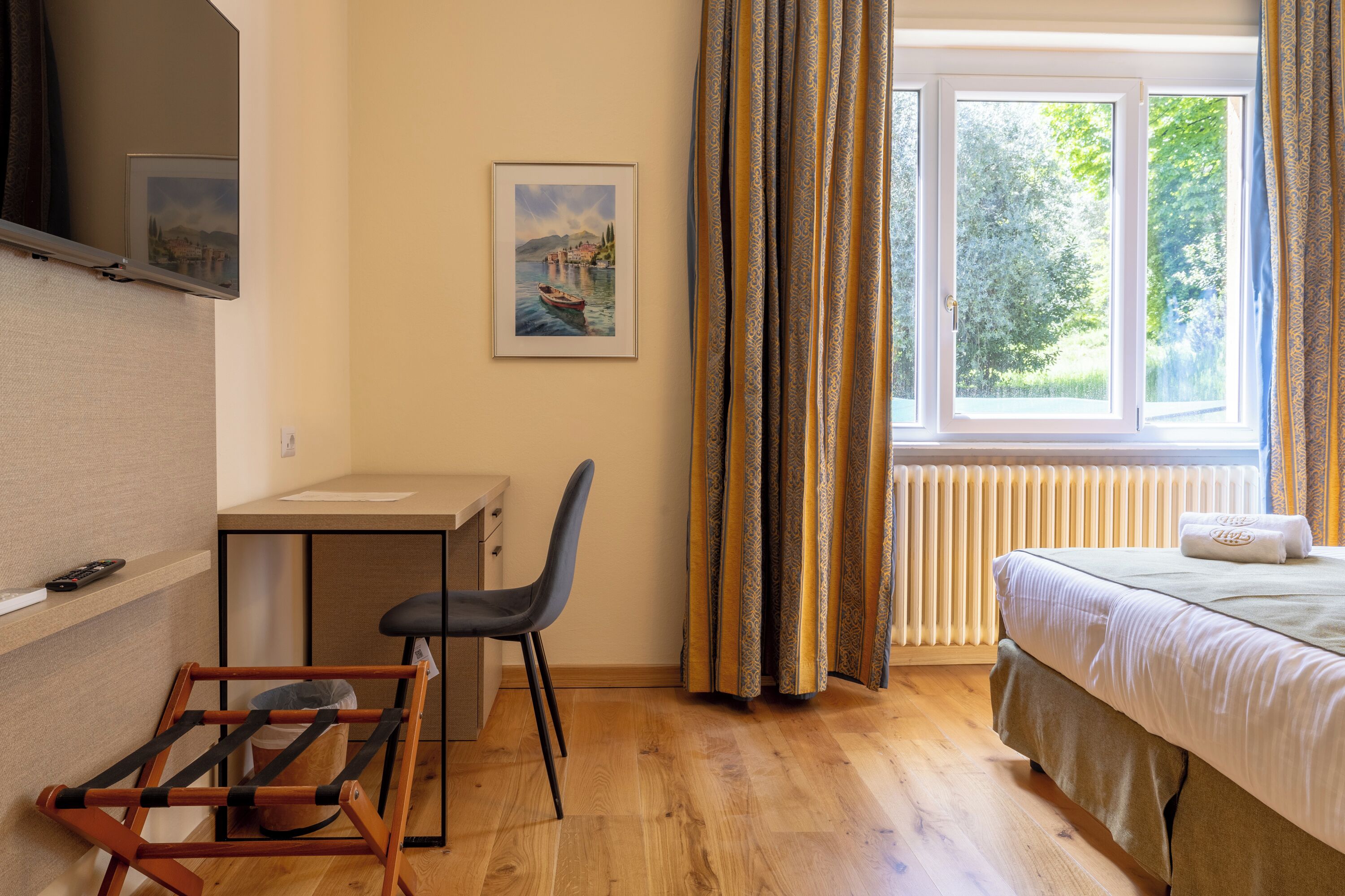 A room with a bed, a desk, a chair, a radiator, and a window with curtains.