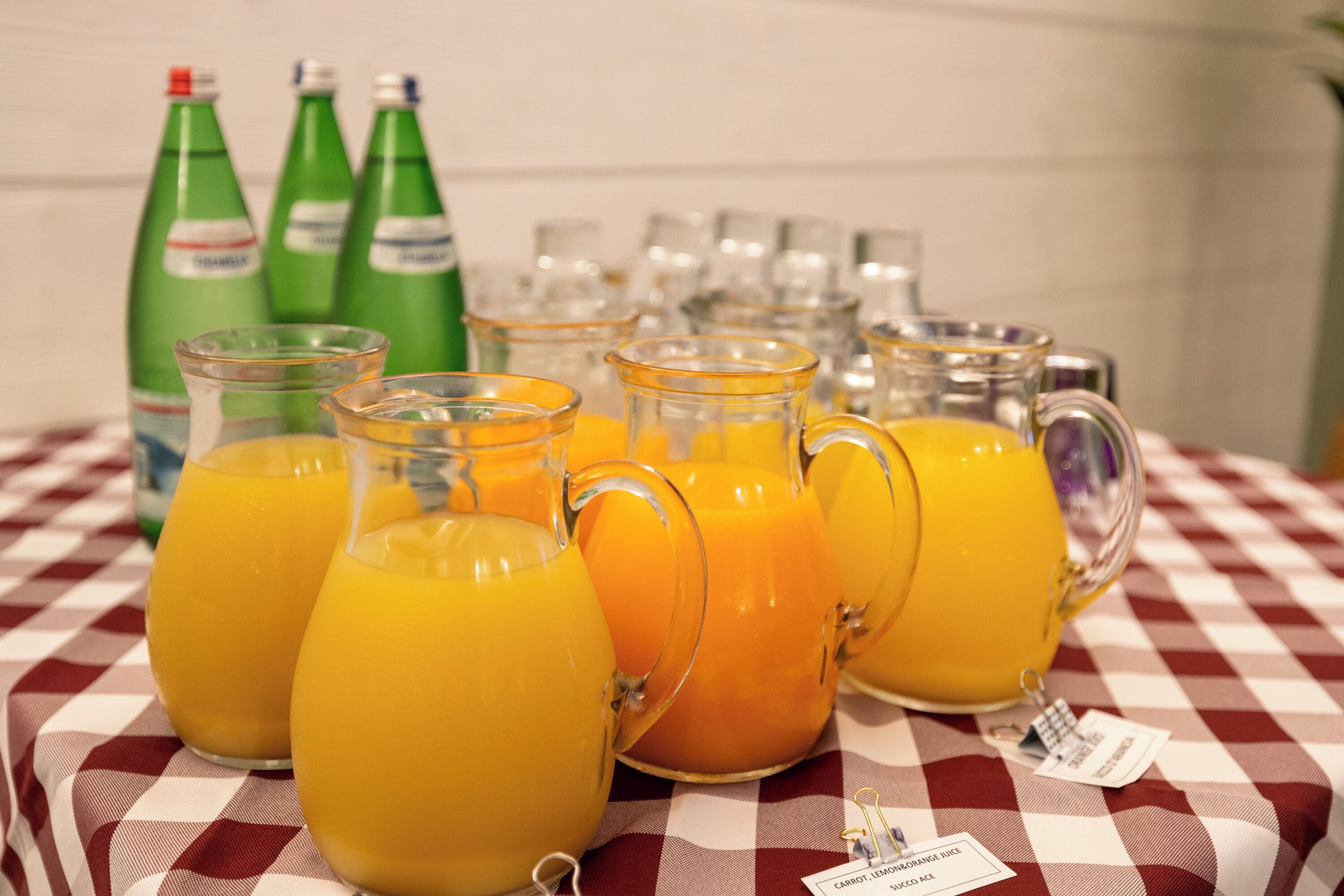 Ein Tisch mit mehreren Gläsern Orangensaft und grünen Limoflaschen.