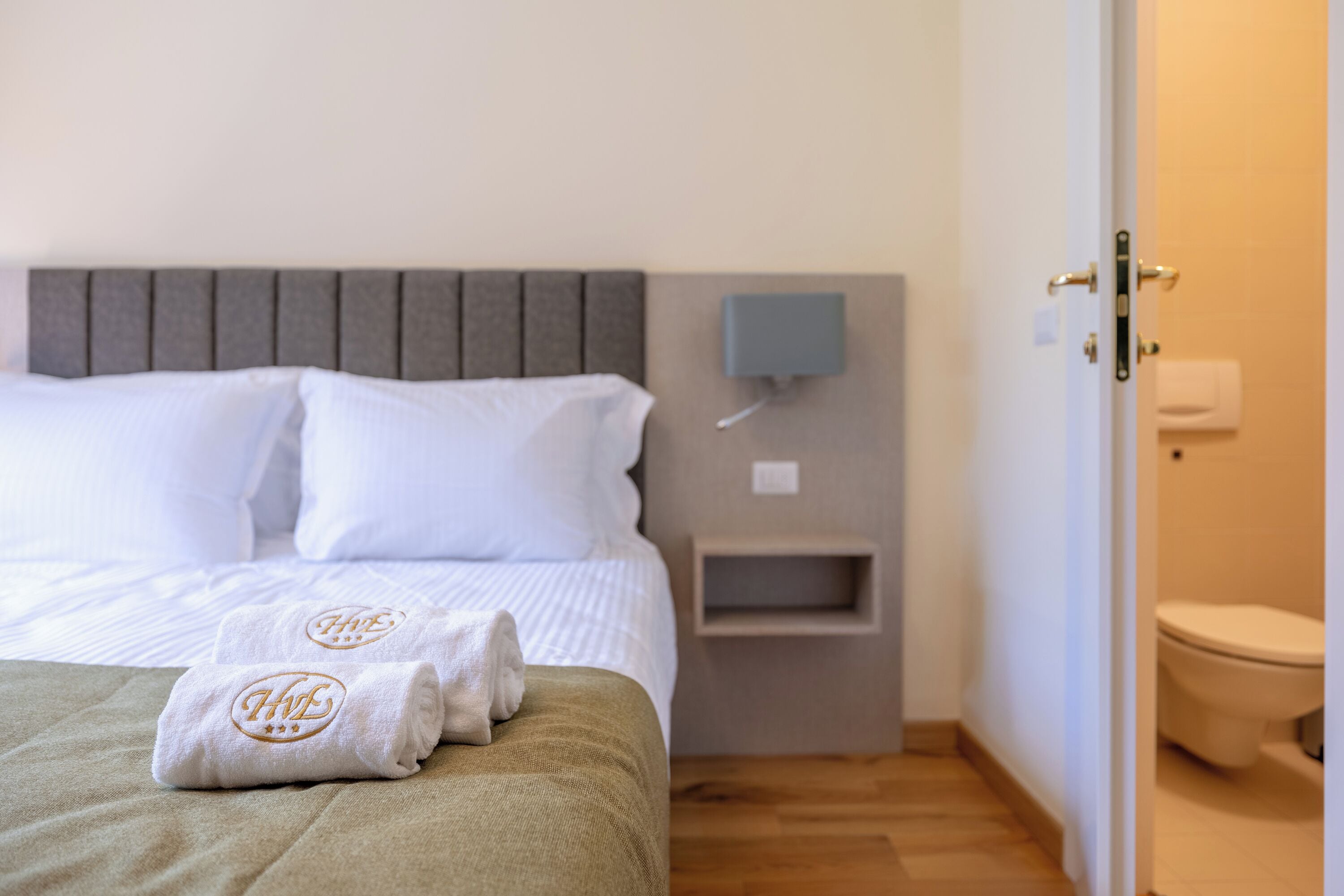 Een hotelkamer met een bed, nachtkastje, wandlamp en toilet.