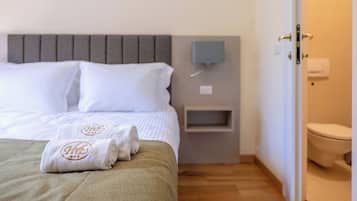 Een hotelkamer met een bed, nachtkastje, wandlamp en toilet.