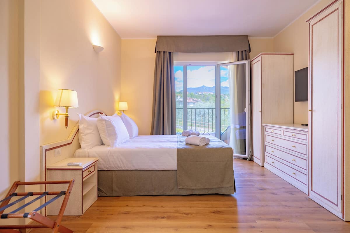A neatly arranged bedroom with a bed, bedside lamps, a wardrobe, and a balcony with a view.