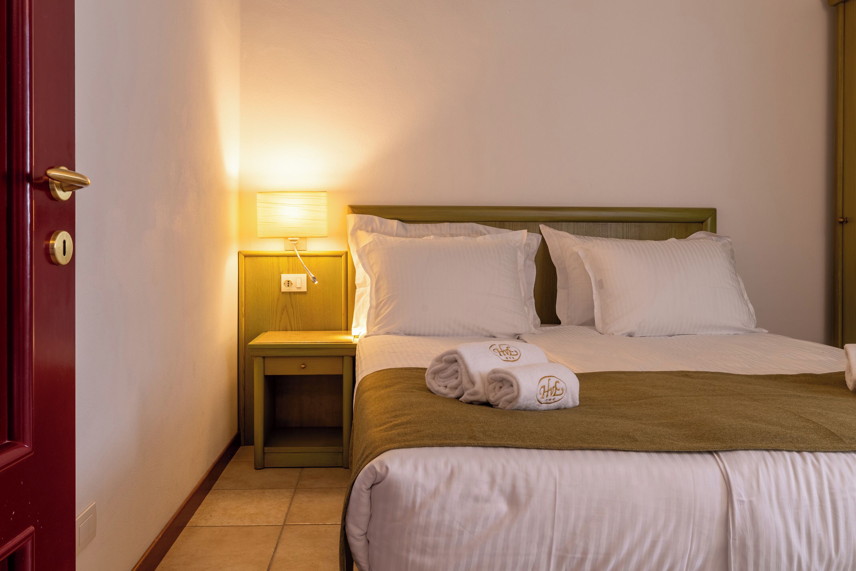 Una camera d'albergo con un letto, un comodino, una lampada e una porta.