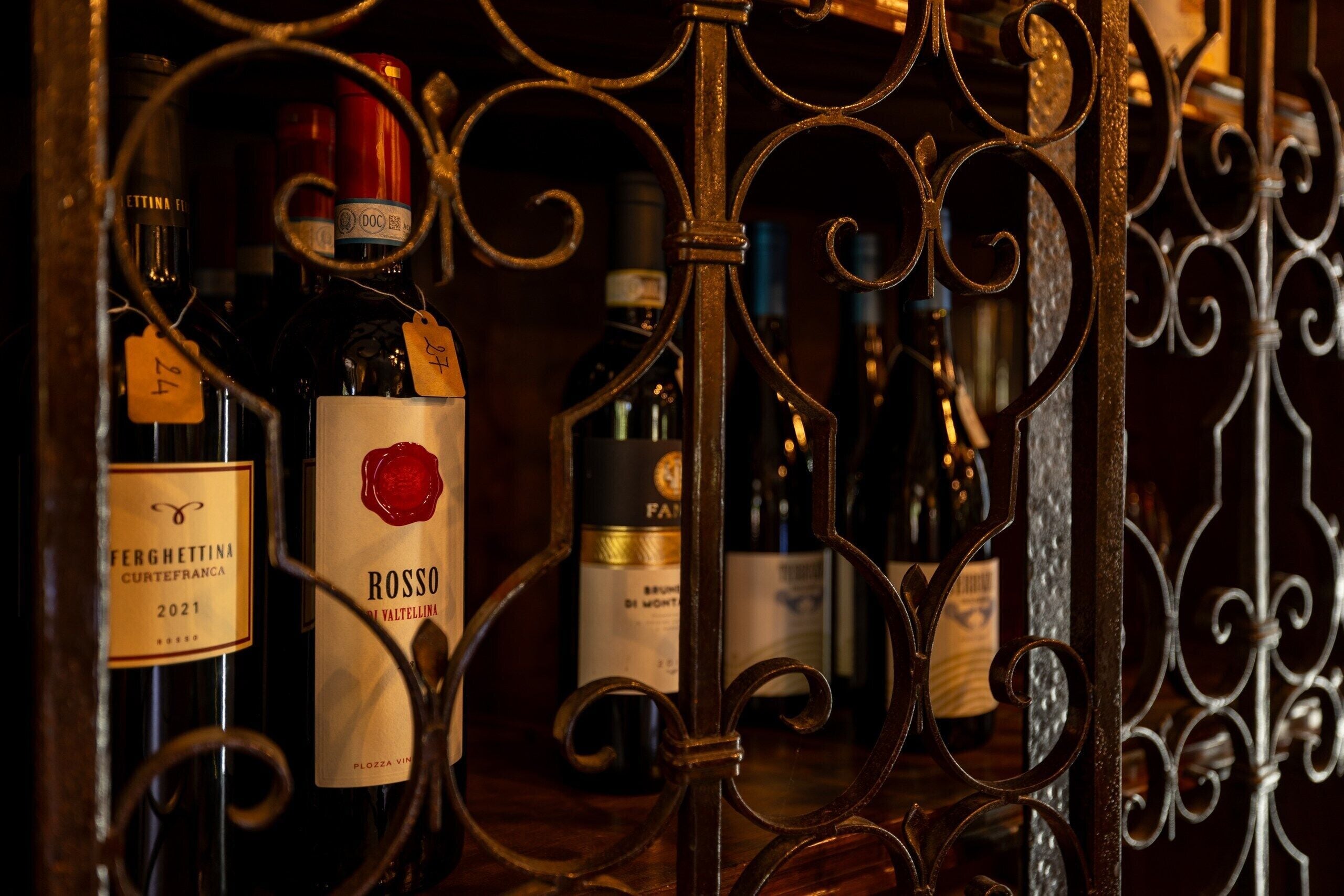 Várias garrafas de vinho em uma estante de metal, com rótulos que indicam diferentes marcas e anos.