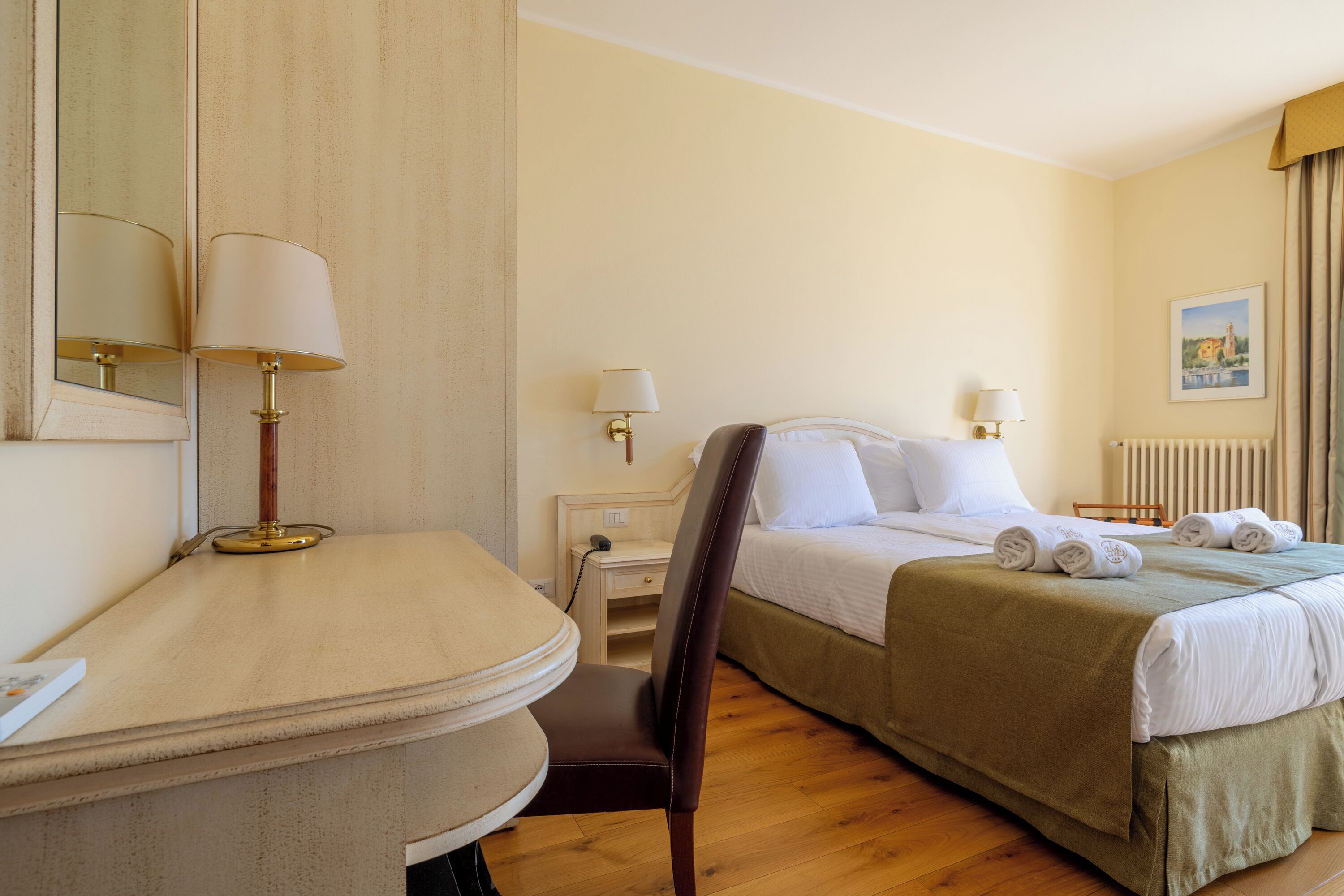 Une chambre d’hôtel comprenant un lit, des tables de chevet, des lampes, une chaise, un bureau et un radiateur.