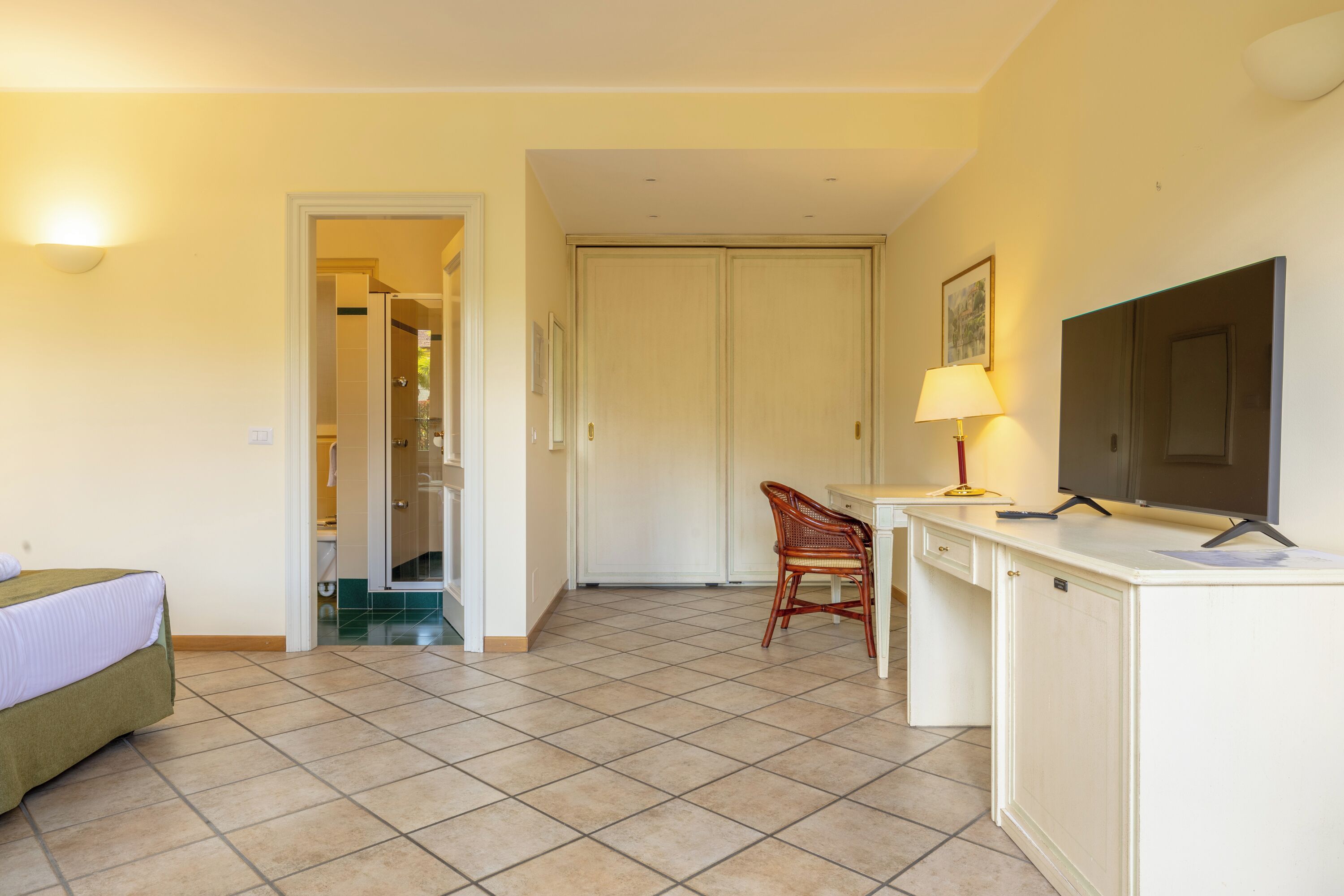A hotel room with a bed, a desk, a chair, a TV, and a door leading to a bathroom.