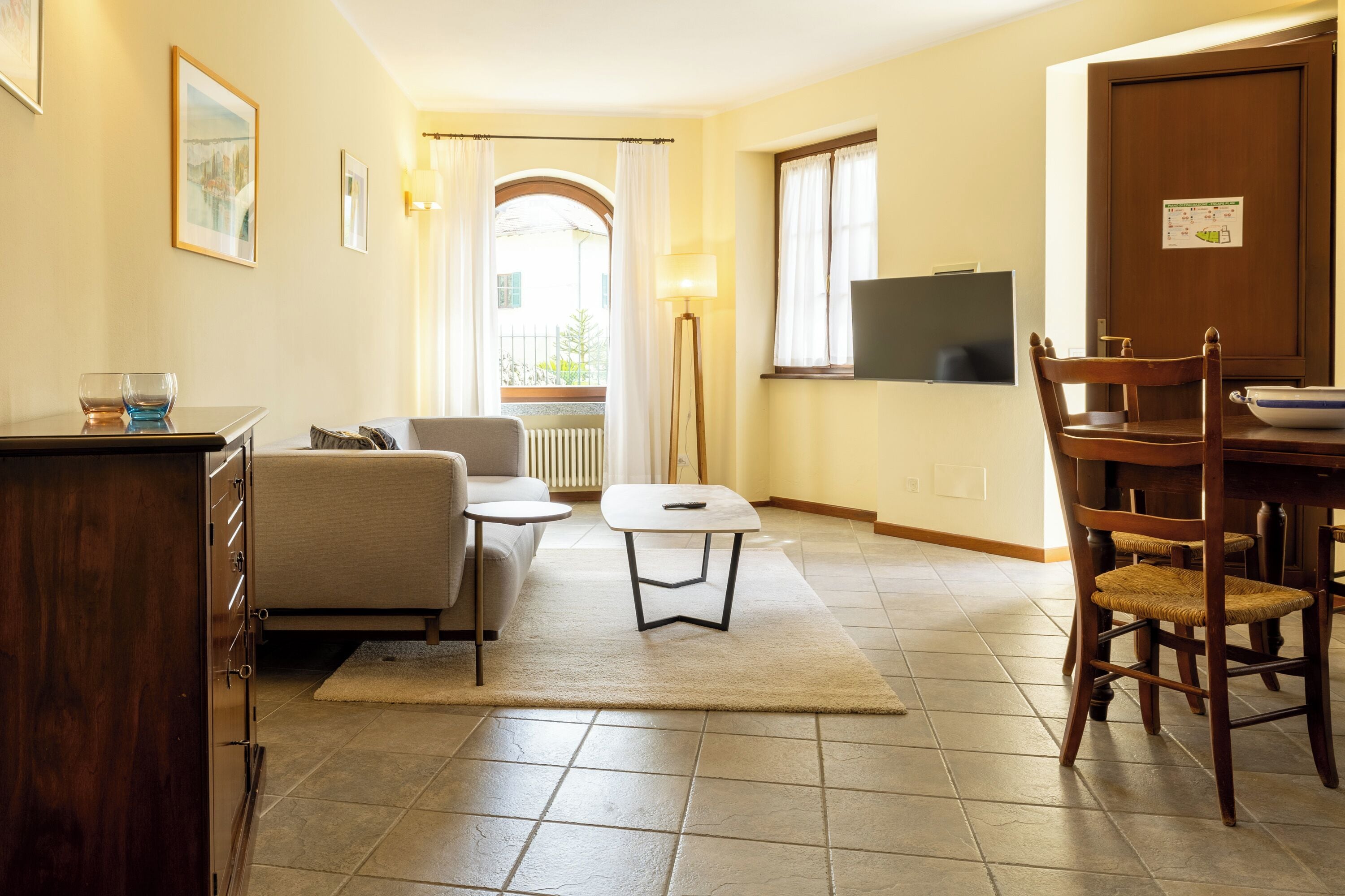 Ein Wohnzimmer mit einer Couch, einem kleinen Tisch, einer Lampe und einem Fernseher an der Wand.