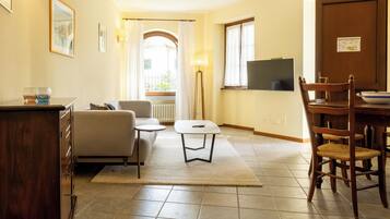 Ein Wohnzimmer mit einer Couch, einem kleinen Tisch, einer Lampe und einem Fernseher an der Wand.
