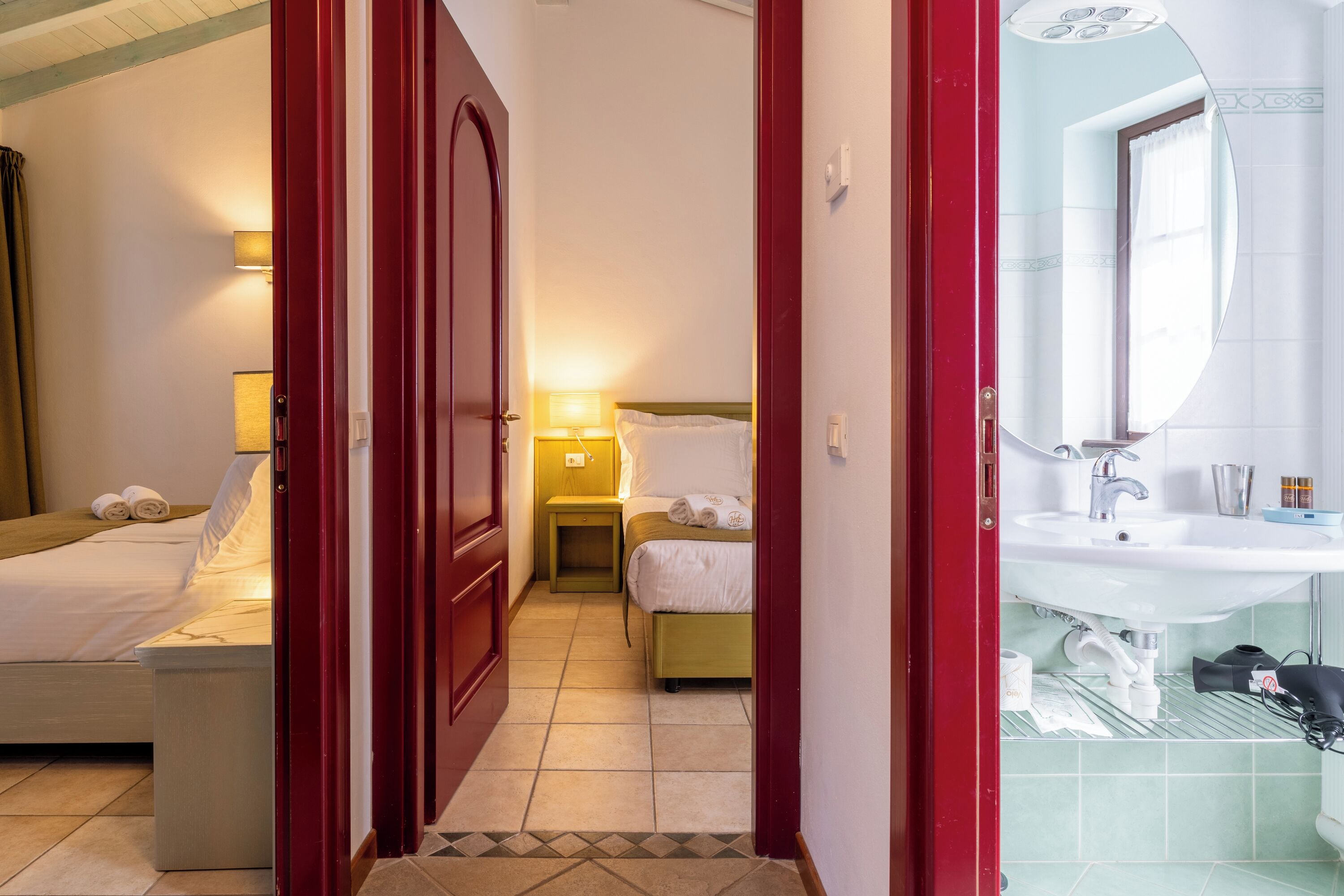 Habitación de hotel con cama, mesita de noche, lámpara y baño con lavabo y espejo.