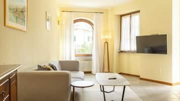 A living room with a sofa, a small round table, a TV mounted on the wall, and a window with curtains.