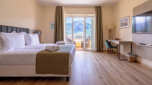 A hotel room with a bed, a desk, a chair, a TV, and a view of mountains. - Hotel Villa Edy (Tremezzina)