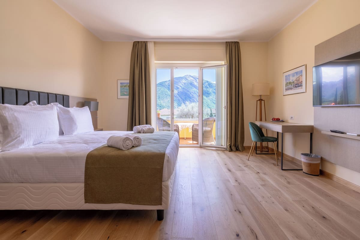A hotel room with a bed, a desk, a chair, a TV, and a view of mountains.