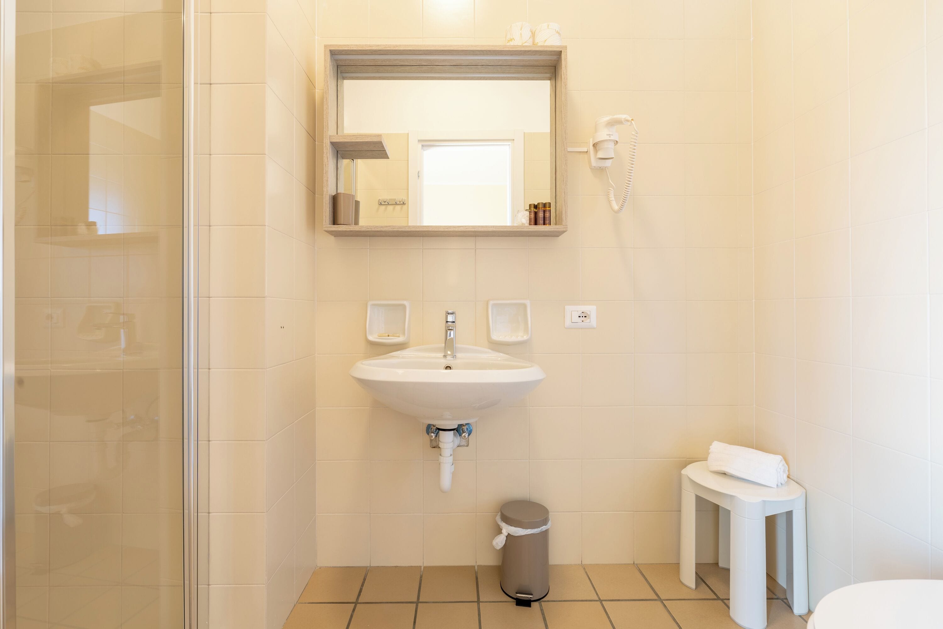 A bathroom with a sink, mirror, and a small stool with a towel.