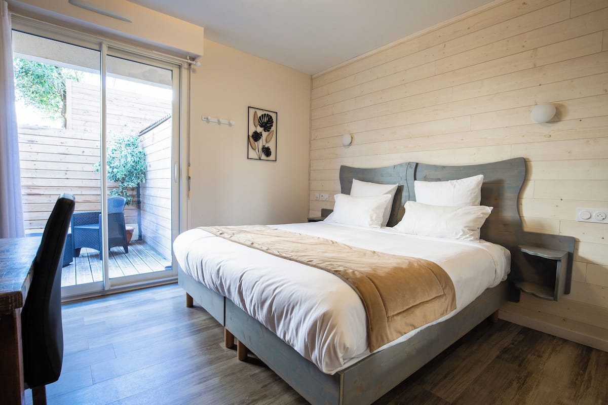 Un dormitorio con cama, una silla, una mesa y un ventanal corredizo que da a un espacio exterior.