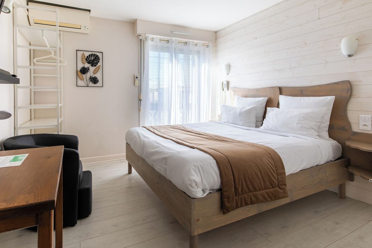 Un dormitorio con una cama de madera, un escritorio con silla, un perchero y una ventana con cortinas.