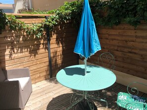Un patio con una mesa redonda, una sombrilla azul, mobiliario de mimbre y una valla de madera con plantas.