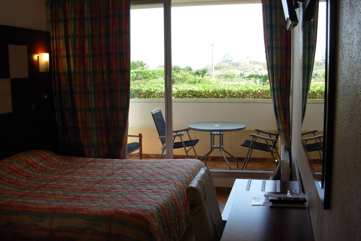 A hotel room with a bed, a small table, and a balcony with chairs and a table.