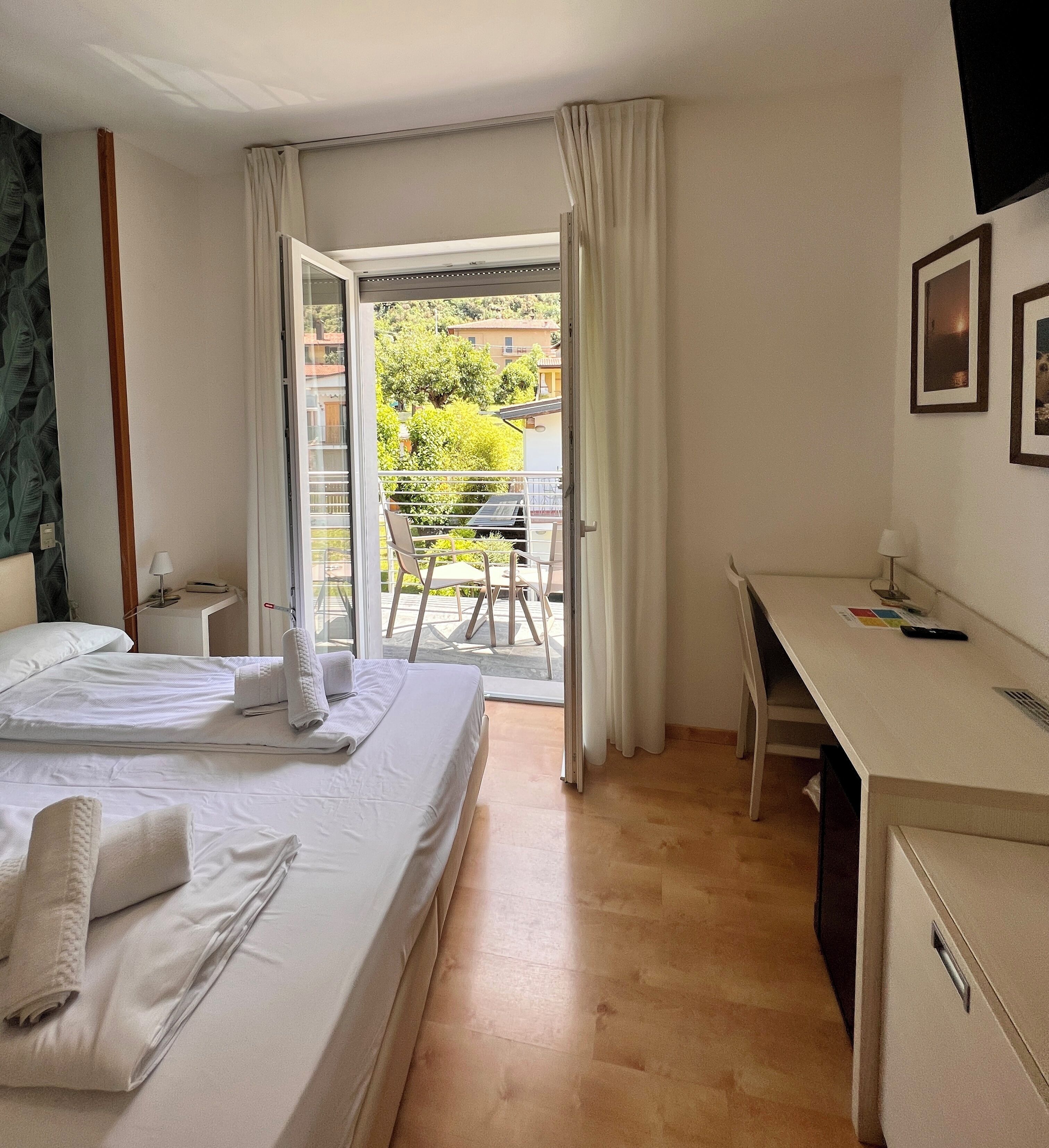 Ein Hotelzimmer mit Bett, Schreibtisch, Stuhl und einem Balkon mit Blick ins Freie.