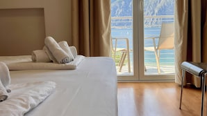 A hotel room with a large bed, a wooden floor, a balcony with a chair, and a mountain view. - San Remo (Malcesine)