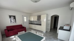 A compact living space with a kitchenette, a dining area with a table and chairs, and a red sofa. - San Remo (Malcesine)