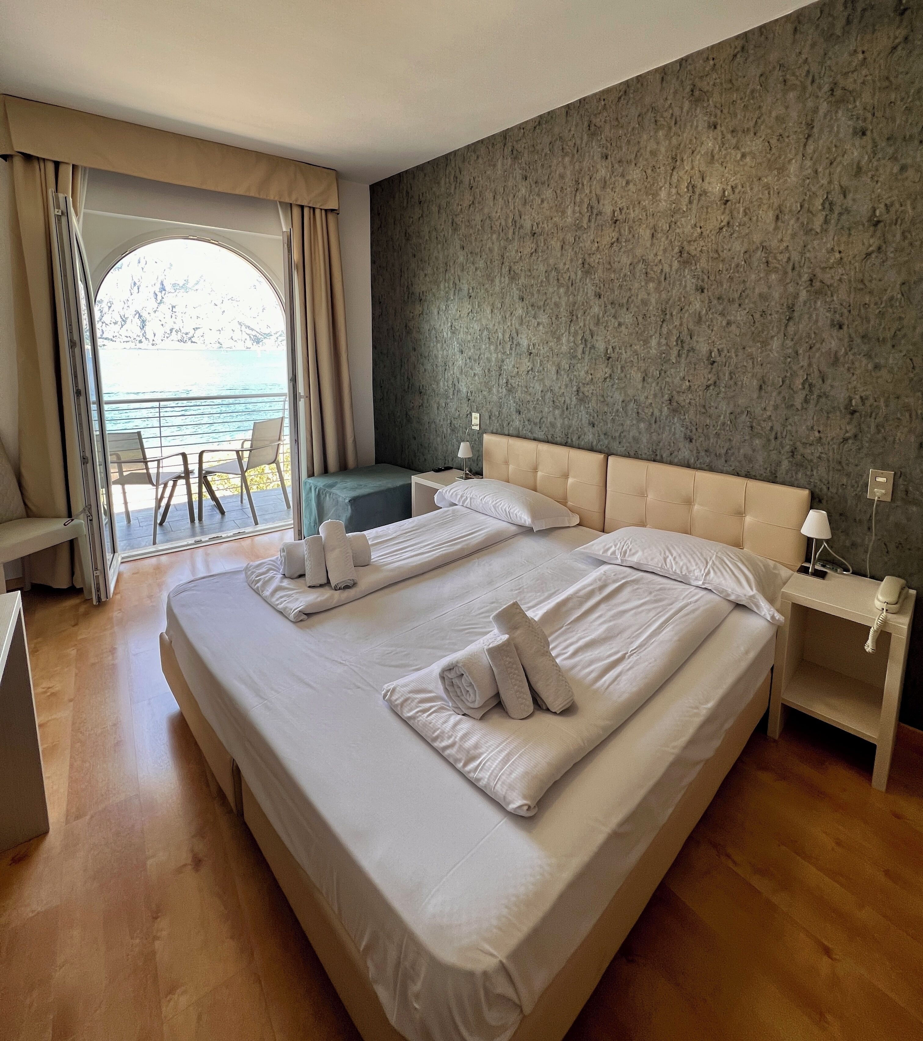 Ein Hotelzimmer mit einem großen Bett, zwei Nachttischen, Meerblick und einem Balkon mit Sitzgelegenheiten.