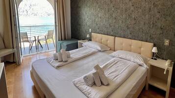 Ein Hotelzimmer mit einem großen Bett, zwei Nachttischen, Meerblick und einem Balkon mit Sitzgelegenheiten.