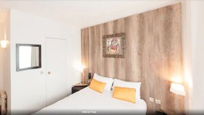 Une chambre d’hôtel avec un lit, une table de chevet, un tableau accroché au mur et une porte.