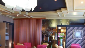 Un espace repas avec des chaises rouges et crème, des tables en bois et un grand lustre.
