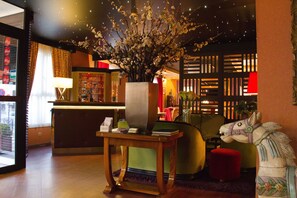 A lobby with a reception desk, a large vase with flowers, a horse sculpture, and a red ottoman. - Hôtel du Trosy Clamart (Clamart)