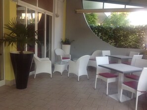 An outdoor patio area with white wicker furniture and a large planter. - Pensione Imperia (Lignano Sabbiadoro)