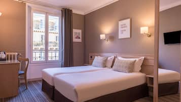 Une chambre d’hôtel avec deux lits, un bureau, une chaise, une fenêtre avec des rideaux et des lampes fixées au mur.
