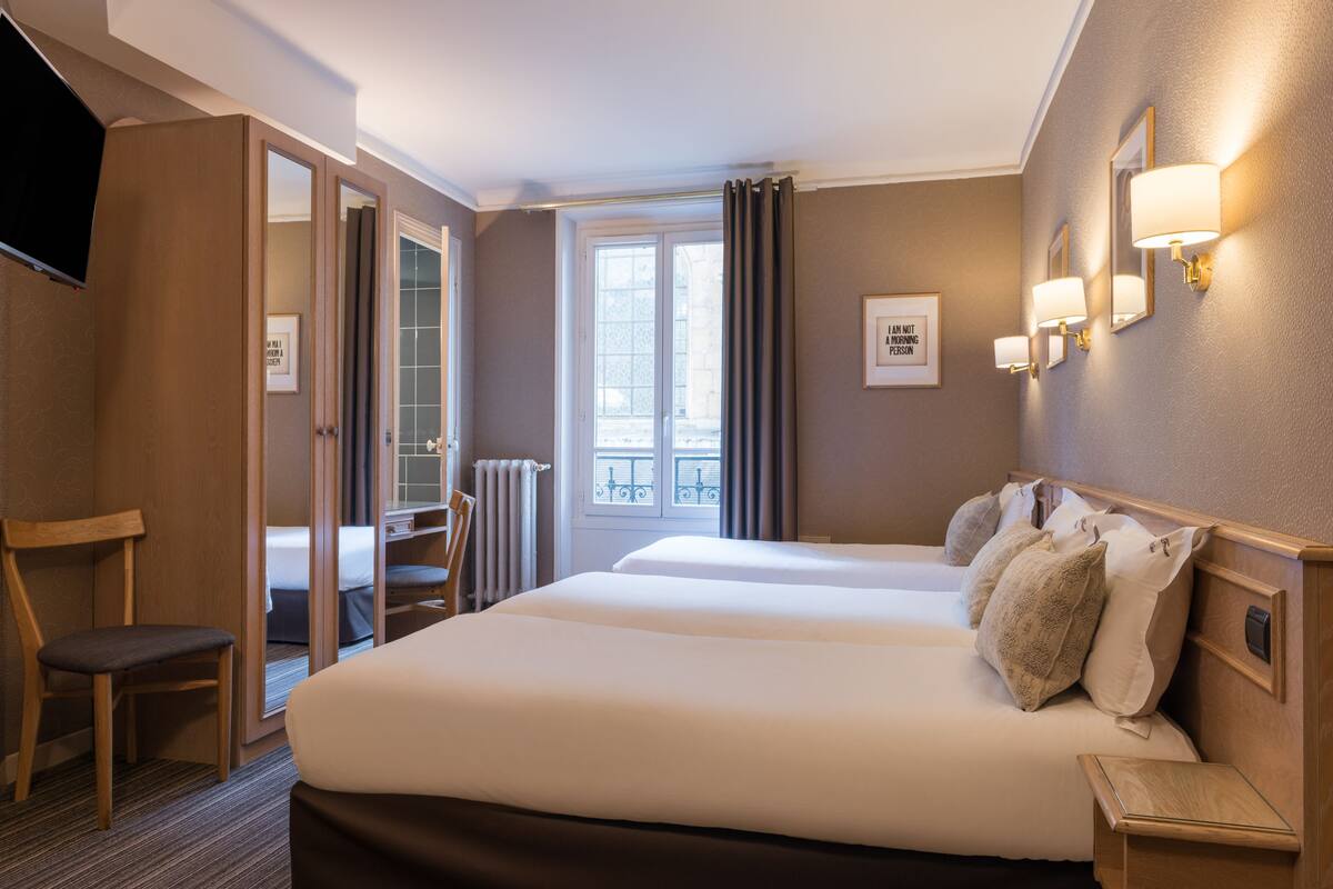 Une chambre d’hôtel avec deux lits, une chaise, un bureau, une télévision et une fenêtre avec des rideaux.