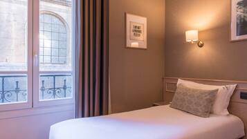 A hotel room with a large window, a framed quote on the wall, a bedside lamp, and a neatly made bed.