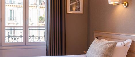 A hotel room with a bed, a framed picture on the wall, and a window with curtains.