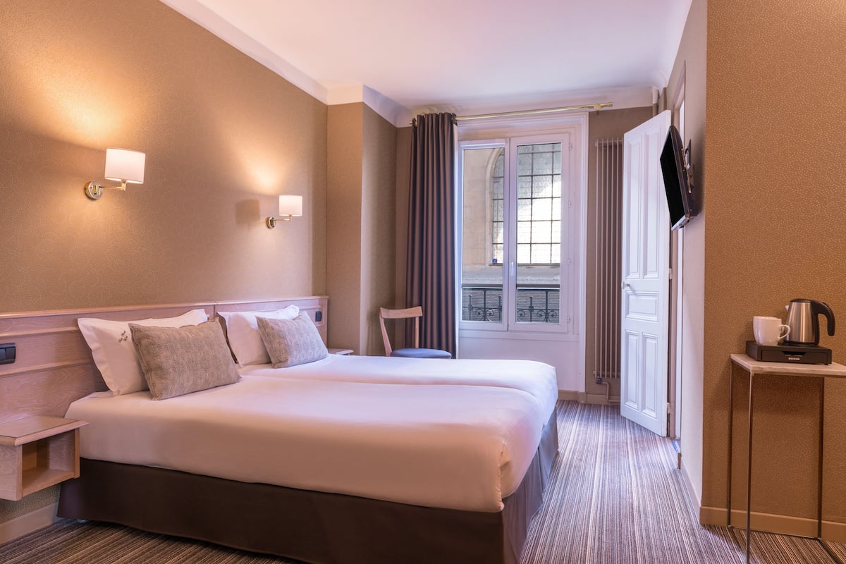 Une chambre d’hôtel avec un grand lit, des tables de chevet, une chaise, un téléviseur et une fenêtre avec des rideaux.