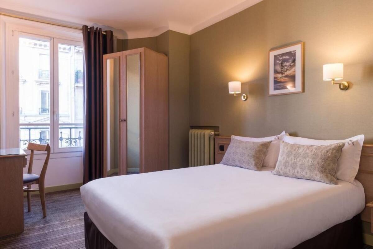 Une chambre d’hôtel avec un lit, une chaise, une armoire, un radiateur et une fenêtre avec des rideaux.