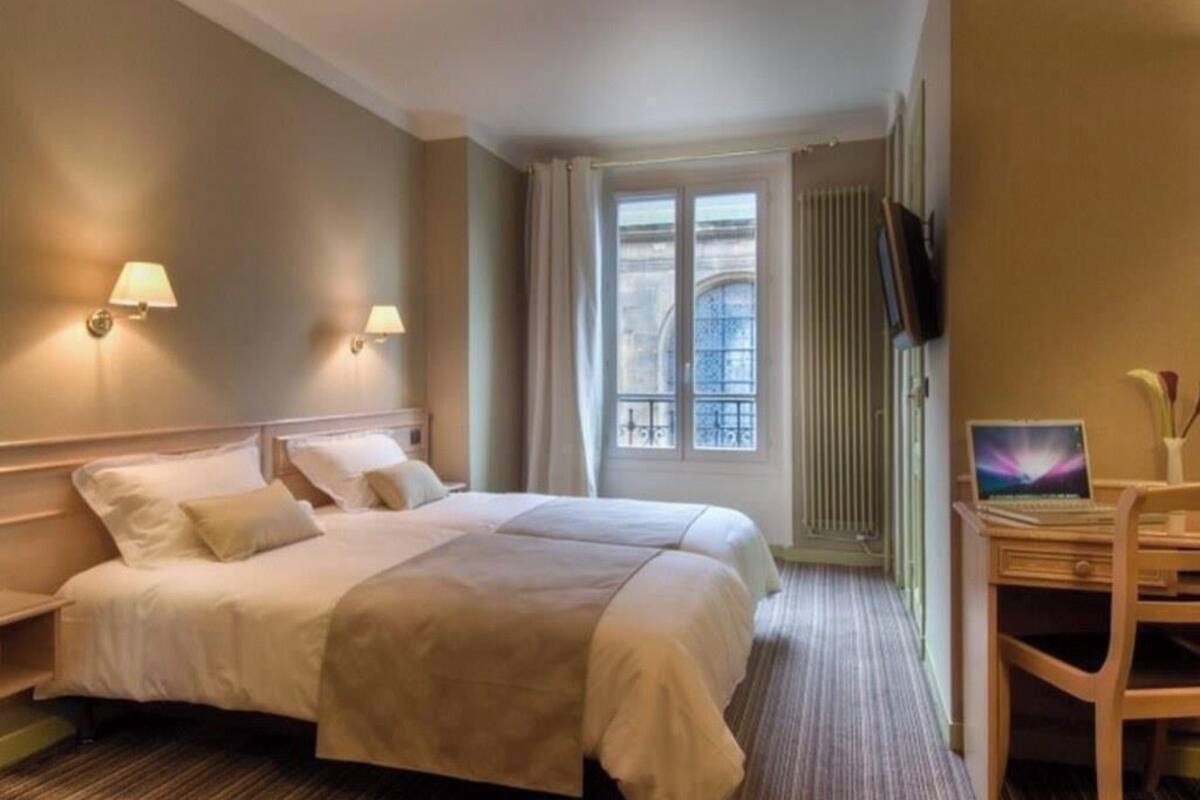 Une chambre d’hôtel avec un lit double, deux lampes de chevet, un bureau avec un ordinateur portable, une fenêtre avec des rideaux et un radiateur.