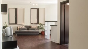 Uma sala de estar moderna com um sofá cinzento, uma televisão de tela plana, uma planta e piso de madeira.