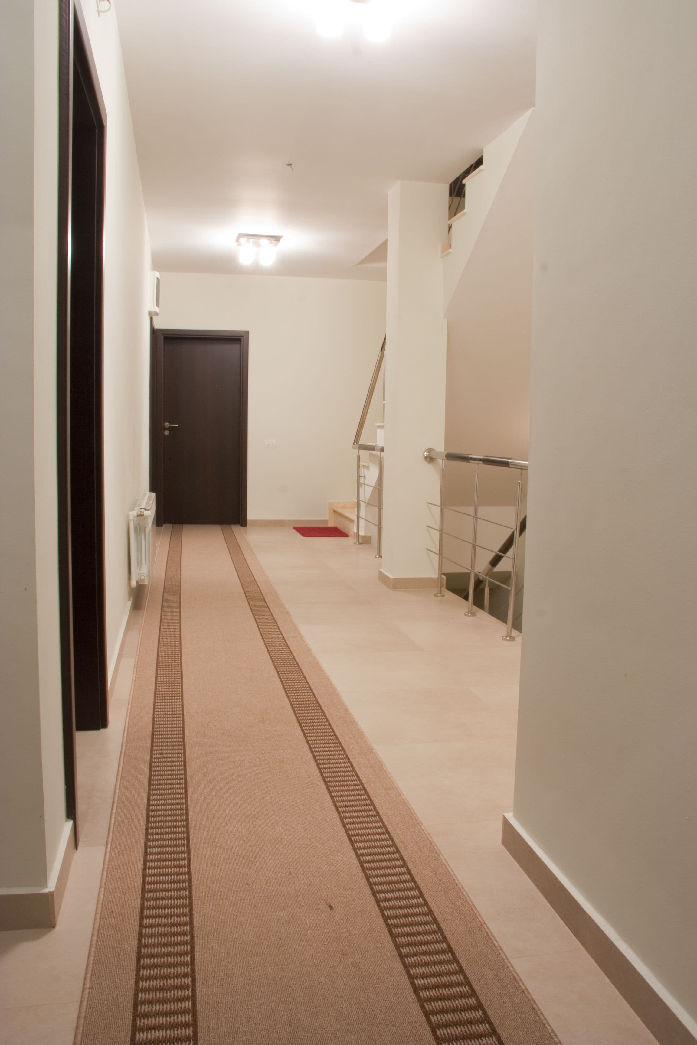 Ein schmaler Flur mit Teppichboden, einer Tür am Ende und einer Treppe zur Rechten.