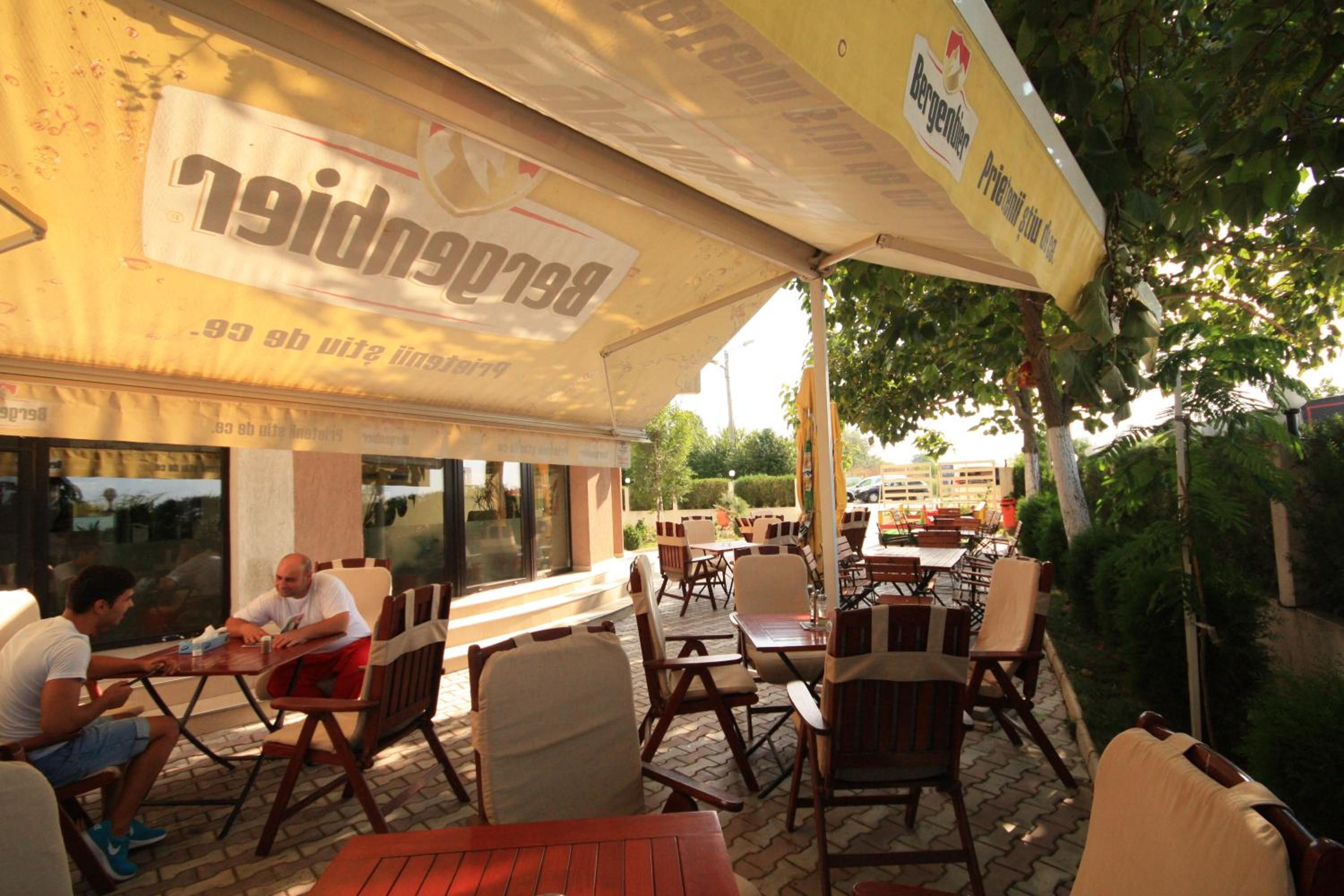 An outdoor café with tables and chairs, a covered seating area, and a building with signage.