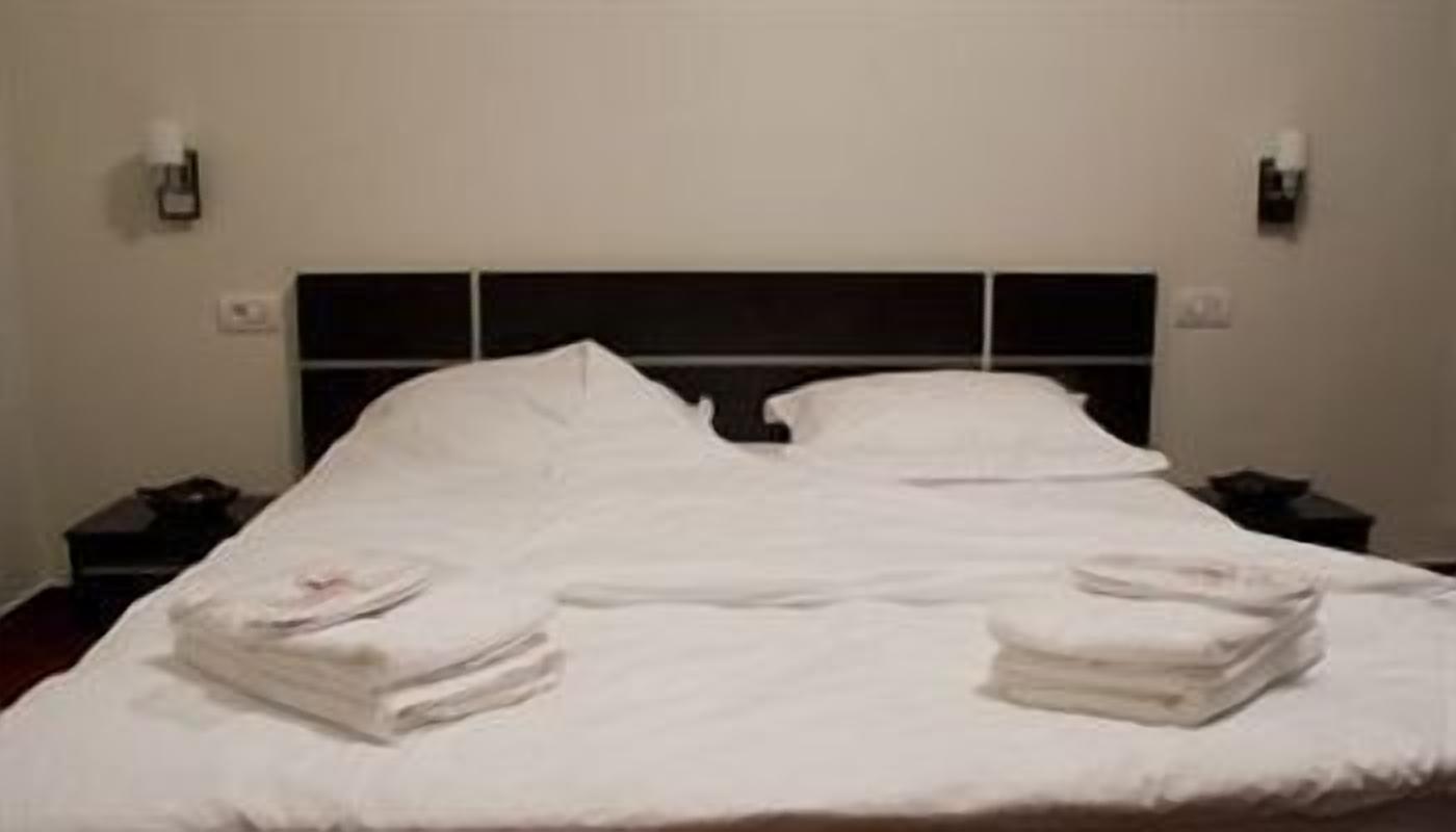 A neatly made bed with white linens and two folded towels on the side.