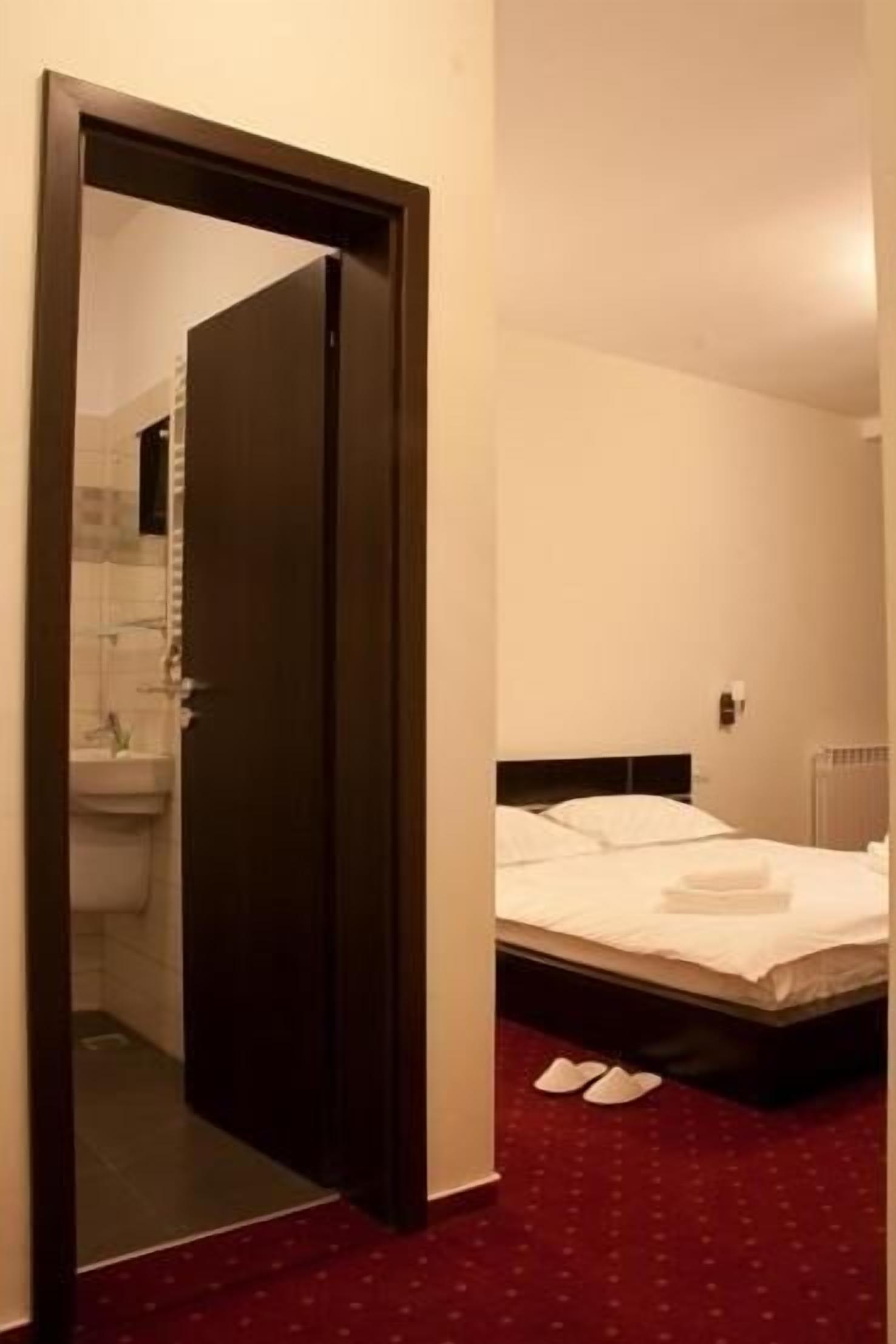 A hotel room with a bed, a bathroom visible through an open door, and a red carpet.