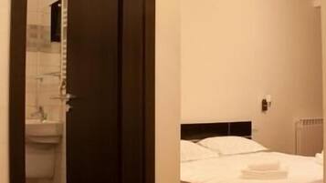 A hotel room with a bed, a bathroom visible through an open door, and a red carpet.