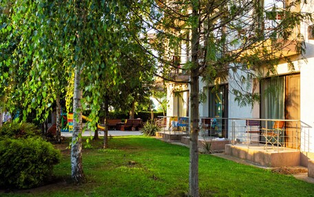A modern building with a covered outdoor seating area, a grassy lawn, and trees.