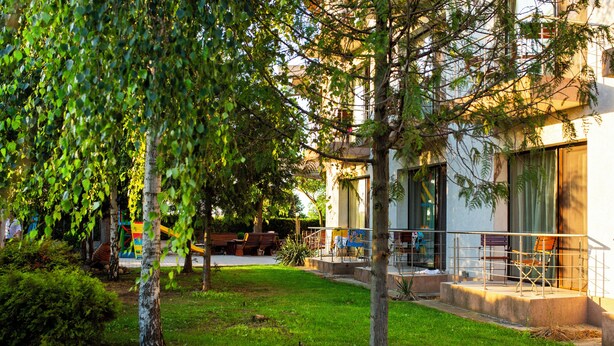 Um edifício moderno com área externa coberta para assentos, gramado e árvores.