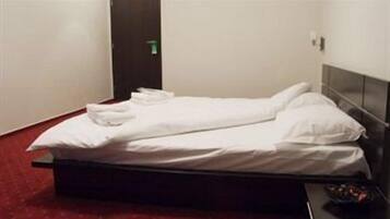 Una cama individual con sábanas blancas, un cabecero oscuro y un suelo cubierto de moqueta roja.